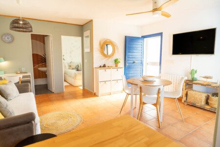 Salón luminoso de Tarifa Cozy House con comedor redondo, sofá y decoración costera, junto a una puerta azul que da acceso a la terraza.