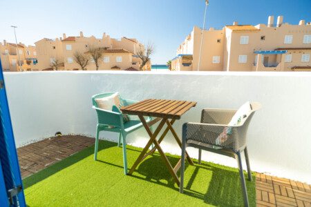 Terraza privada de Tarifa Cozy House con mesa de madera, sillas de colores y césped artificial, con vistas a la playa.