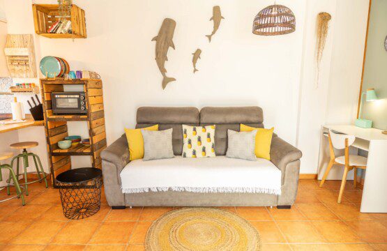 Salón de Tarifa Cozy House con sofá cómodo, escritorio para trabajar, decoración rústica en madera y temática marina con figuras de tiburón en la pared.