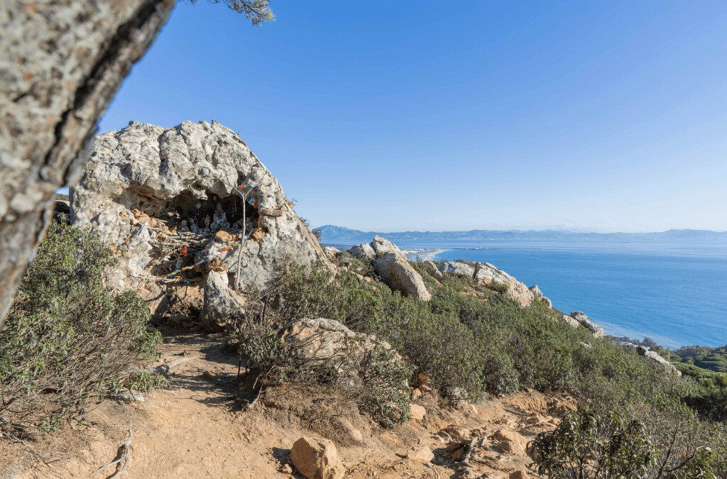 Ruta del Buda en Tarifa – Mirador con vistas al Estrecho de Gibraltar y santuario espiritual en La Peña. Santuario del Buda en la Ruta del Buda de Tarifa, un altar con figuras de Buda decoradas con ofrendas y banderas tibetanas. Vista panorámica del mar Mediterráneo y el Estrecho de Gibraltar desde La Peña, Tarifa.