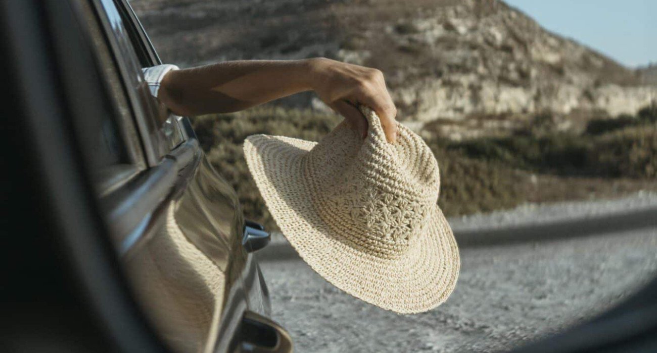 mujer-sosteniendo-el-sombrero-por-la-ventana-en-la-vista-del-espejo-de-coche
